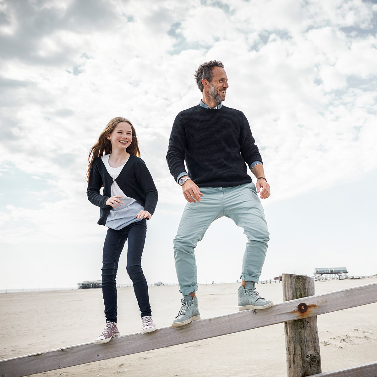 Mann und Mädchen stehen auf einem Holzbalken am Meer