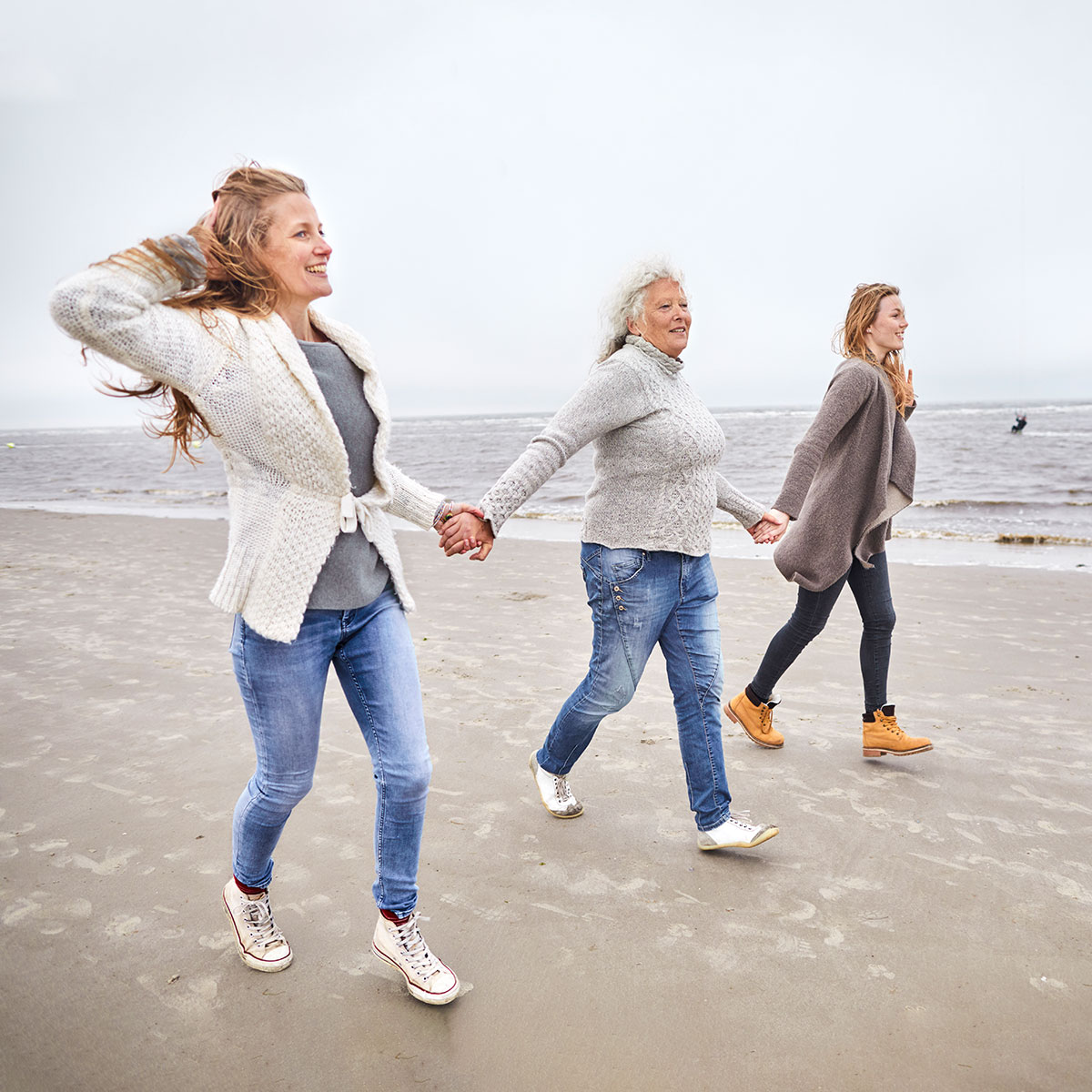 Drei Frauen laufen Hand in Hand am Strand