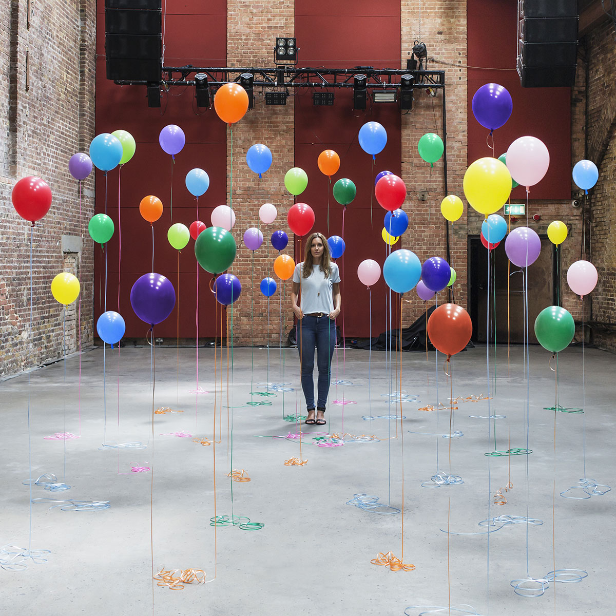Frau in Industriehalle vor vielen bunten Luftballons