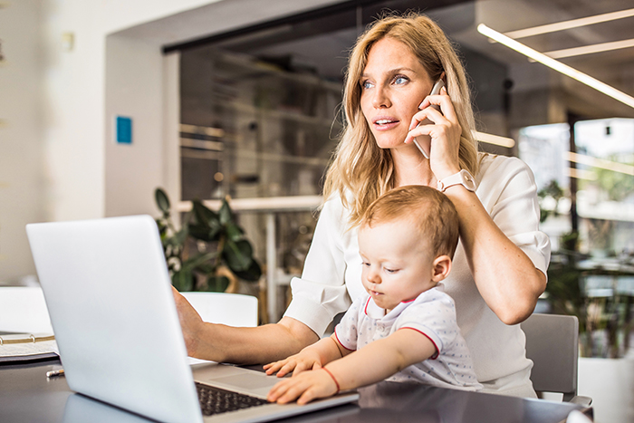 Frau telefoniert mit Kind auf dem Schoß und sitzt am Laptop