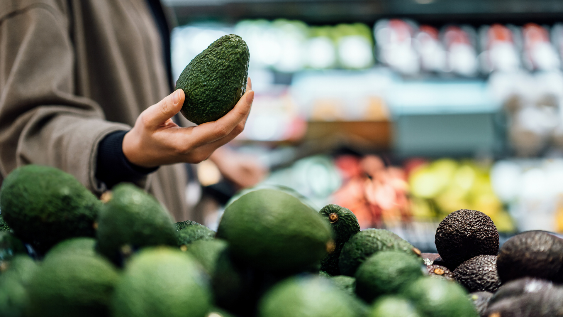 Frau sucht sich eine Avocado im Supermarkt aus