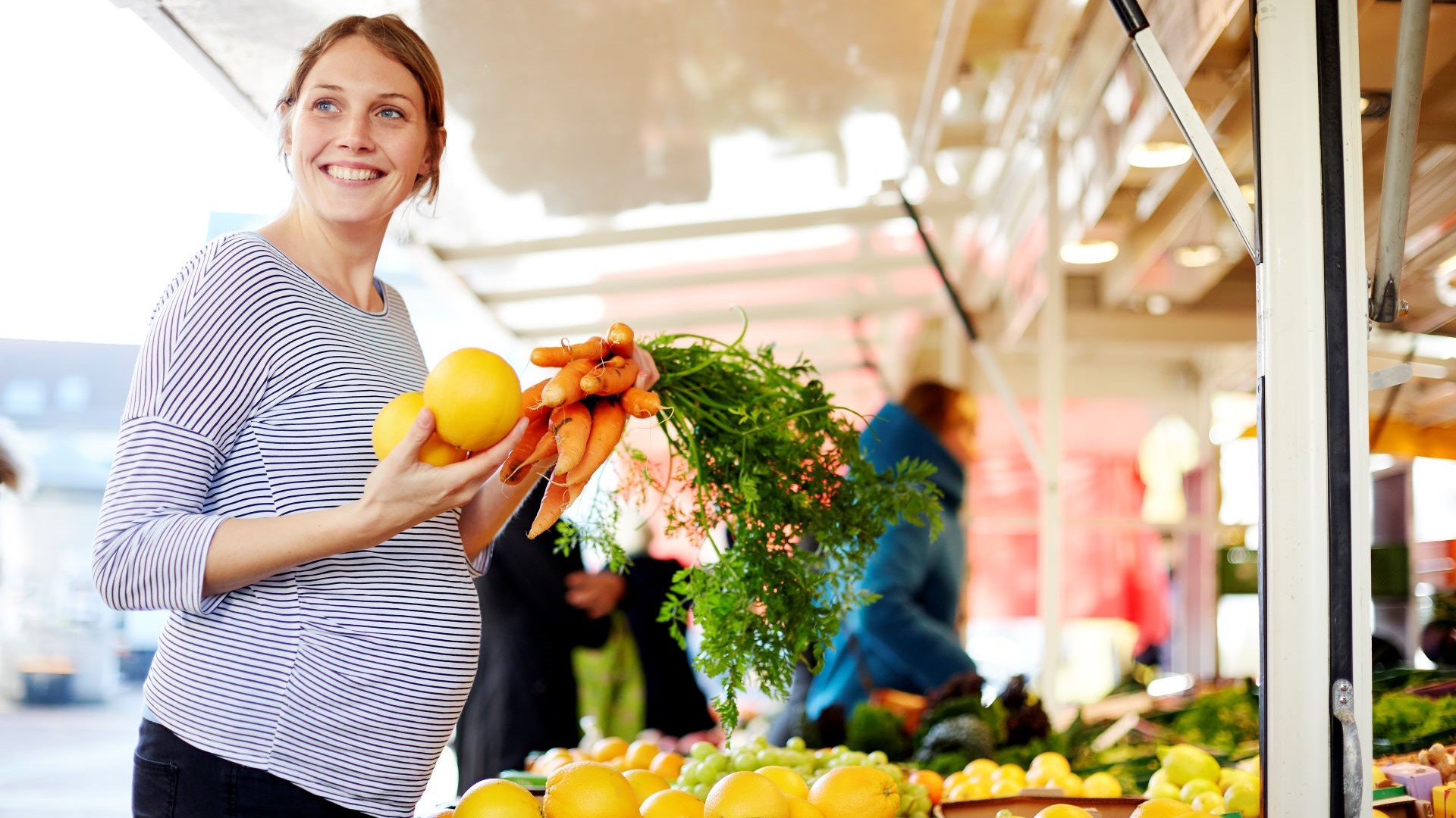 Schwangere Frau lächelt und kauft Obst und Gemüse