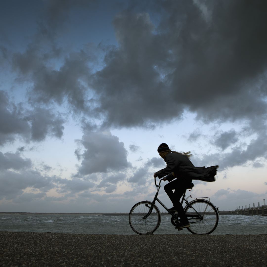 Frau fährt in der Dämmerung mit dem Fahrrad am Meer entlang